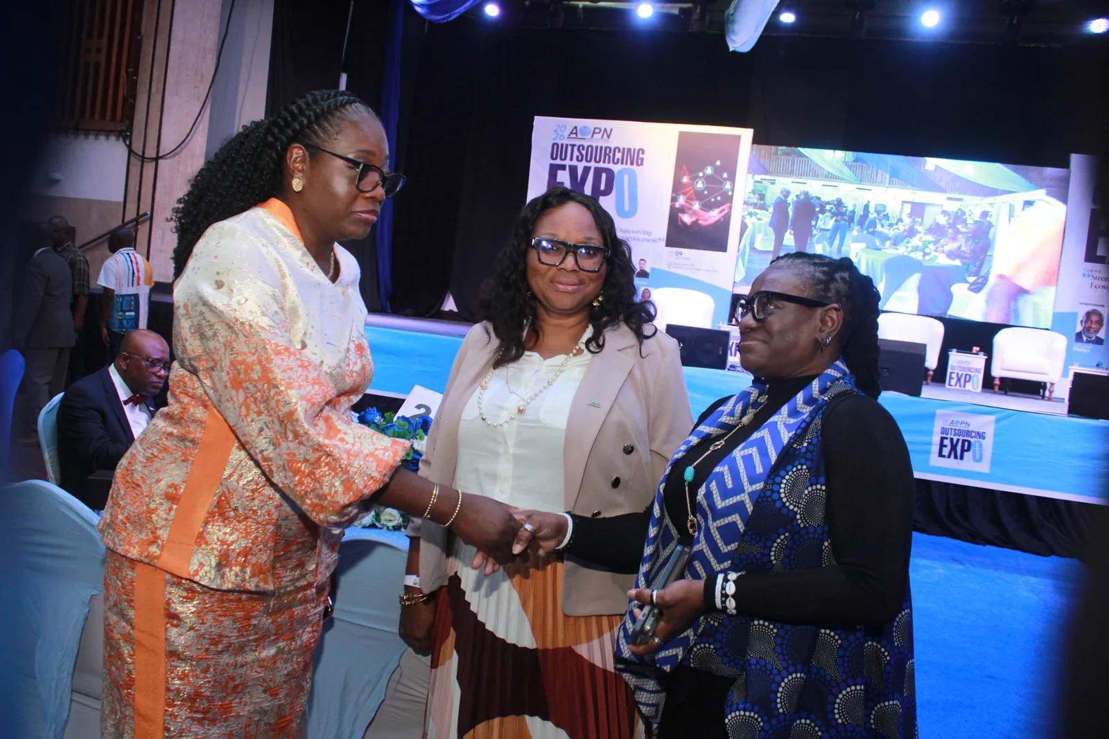Three professional women connecting beside the Outsourcing Expo 2026 stage